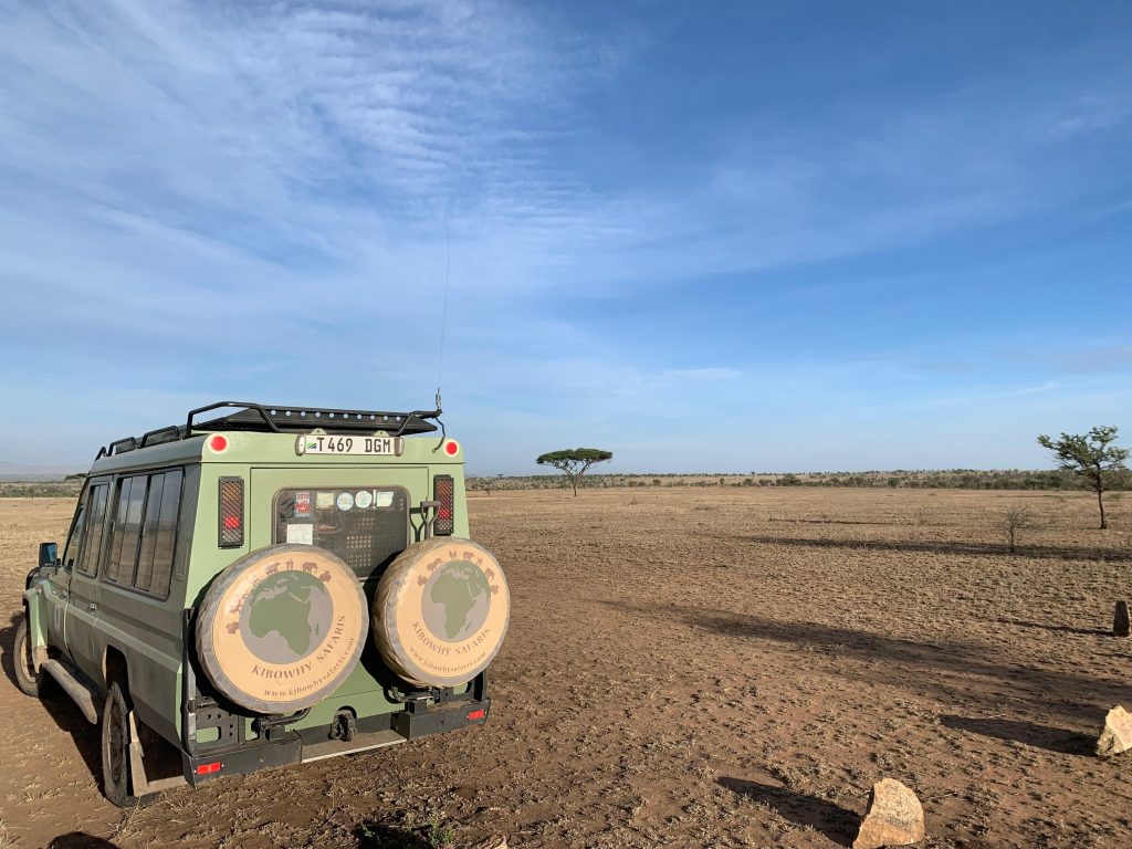 Véhicule Kibowhy Safaris vu de dos dans les grandes étendues de savane en Tanzanie